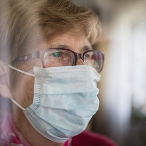 Seniorin mit Mundschutz schaut aus dem Fenster